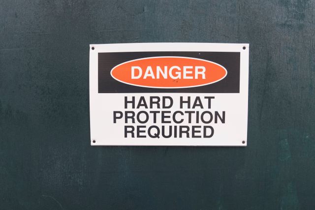 A photo of a warning sign that reads "DANGER, HARD HAT PROTECTION REQUIRED"